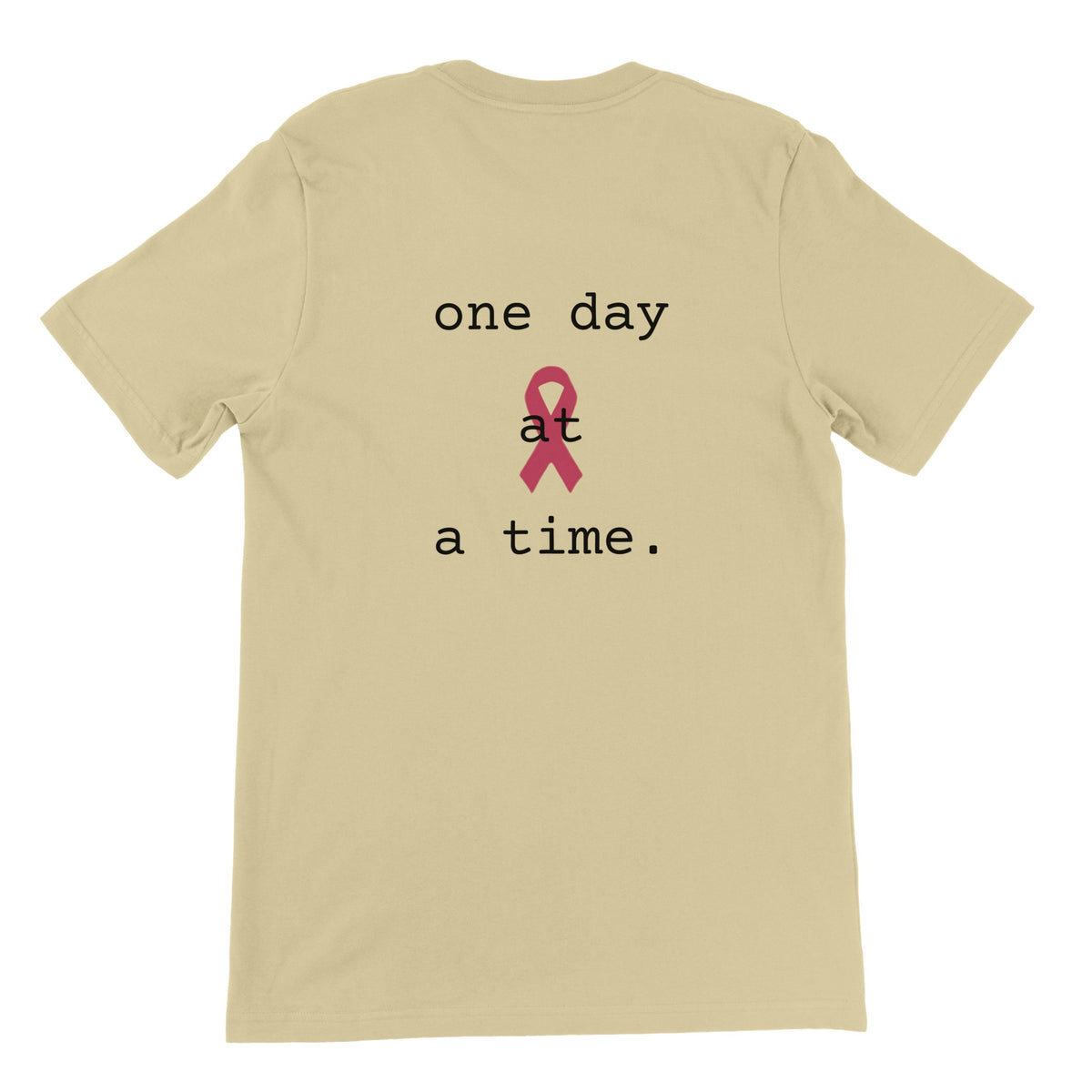 A natural colored short-sleeve t-shirt with a graphic on the front reading 'one day at a time.' in white text, featuring a pink awareness ribbon in the center of the words
