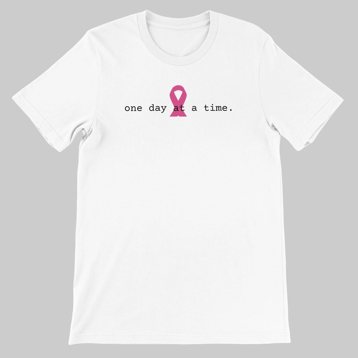 A  white t-shirt with a pink awareness ribbon and the text 'one day at a time.' on a warm grey background
