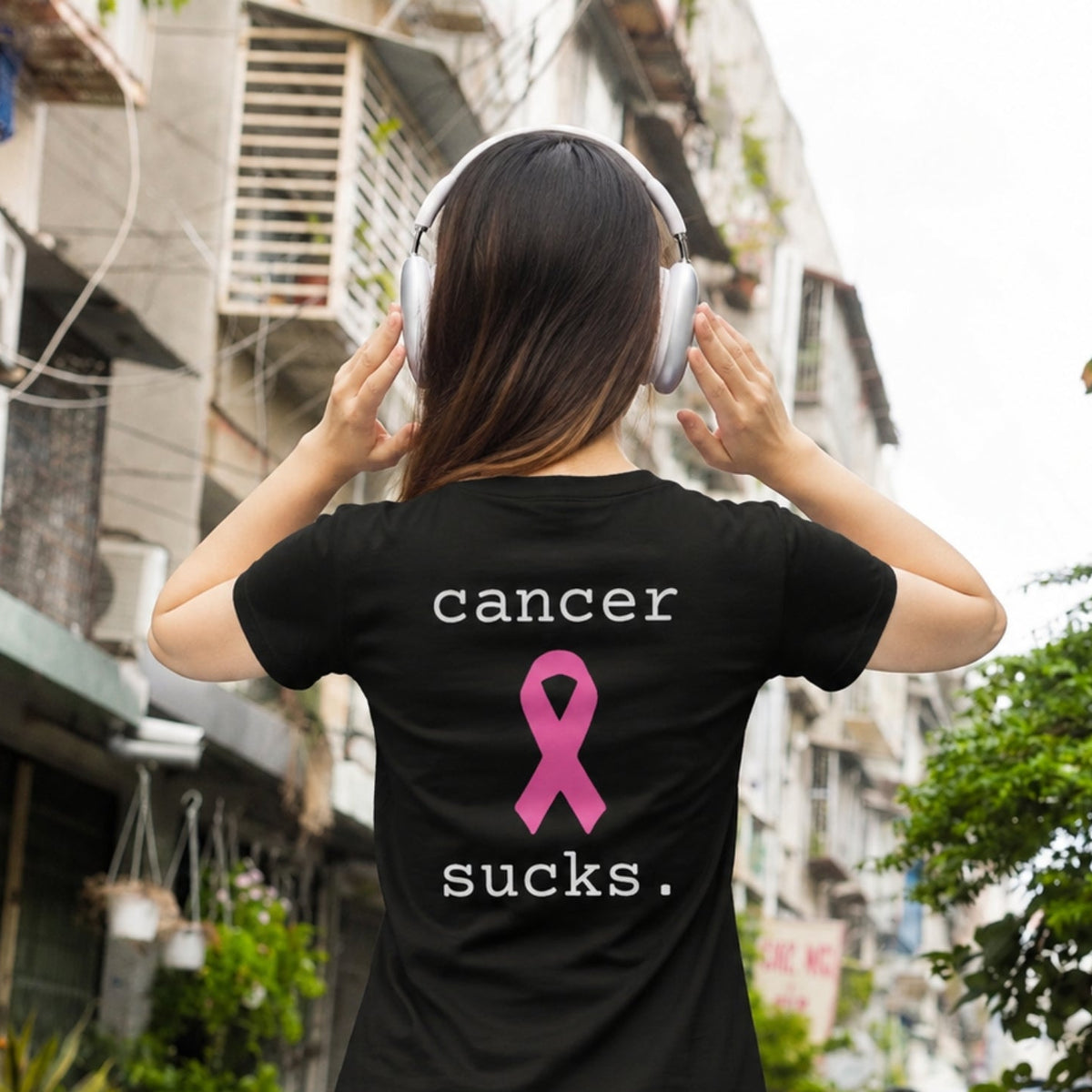 A woman viewed from behind wearing a black t-shirt with a pink ribbon graphic and the text 'cancer sucks.' printed on the back.