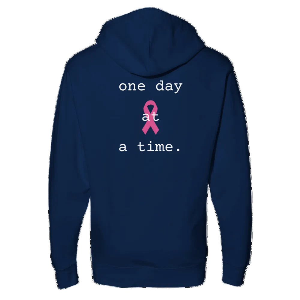 A classic navy blue hoodie shown from the back, featuring a pink breast cancer ribbon and the white text 'one day at a time.' printed on the center back.